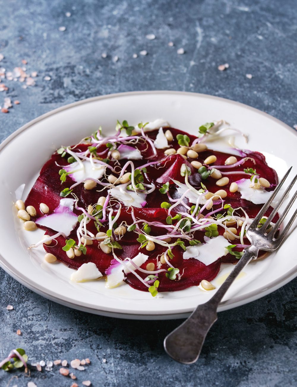 Vegetarian beetroot carpaccio salads with olive oil, goat cheese, pine nuts and sprouts in white plate over blue texture background. Close up. Healthy eating